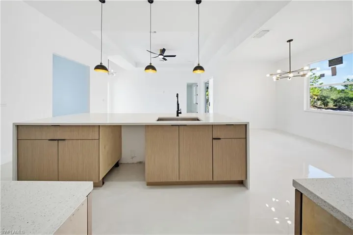 Kitchen with light stone countertops, modern cabinets, a raised ceiling, hanging light fixtures, and a chandelier