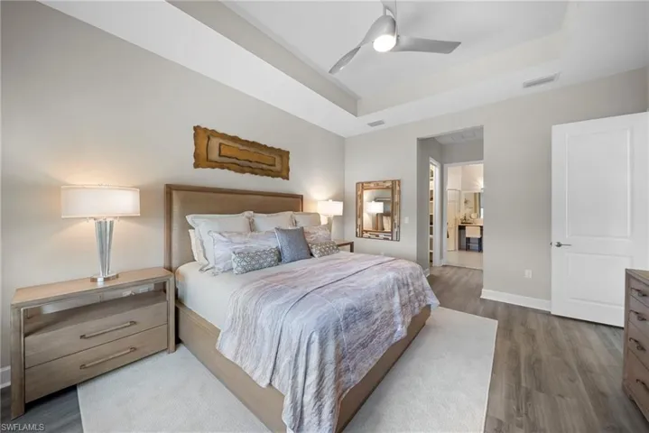 Bedroom featuring a raised ceiling, dark wood-style floors, ensuite bathroom, and a ceiling fan