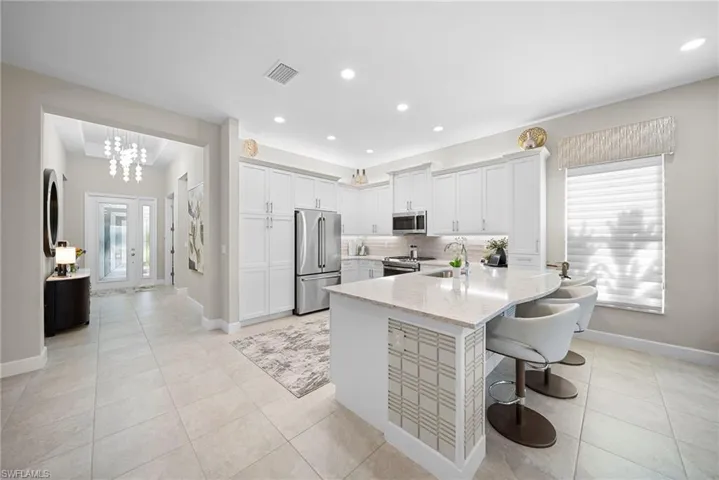Kitchen with white cabinetry, stainless steel appliances, a kitchen bar, a peninsula, and light stone counters