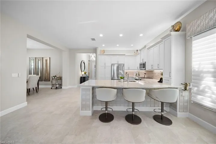 Kitchen with a kitchen bar, a peninsula, light stone counters, white cabinets, and stainless steel appliances