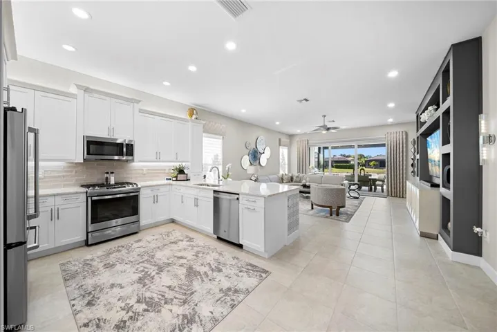 Kitchen with stainless steel appliances, a peninsula, open floor plan, white cabinets, and light stone countertops