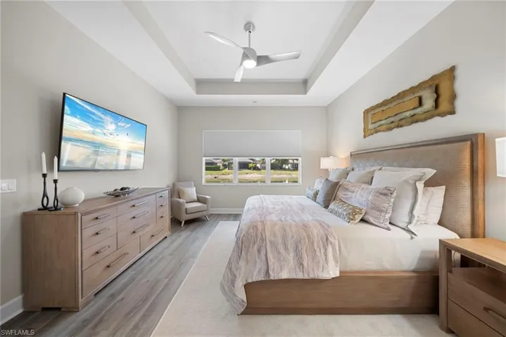 Bedroom with light wood finished floors, ceiling fan, and a tray ceiling