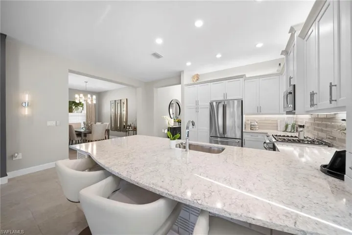 Kitchen featuring a peninsula, a kitchen bar, light stone countertops, backsplash, and stainless steel appliances