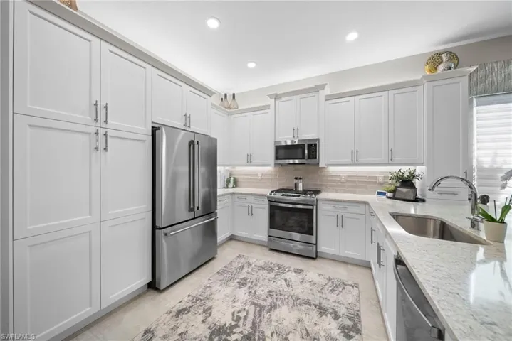 Kitchen featuring stainless steel appliances, light stone counters, white cabinets, recessed lighting, and tasteful backsplash