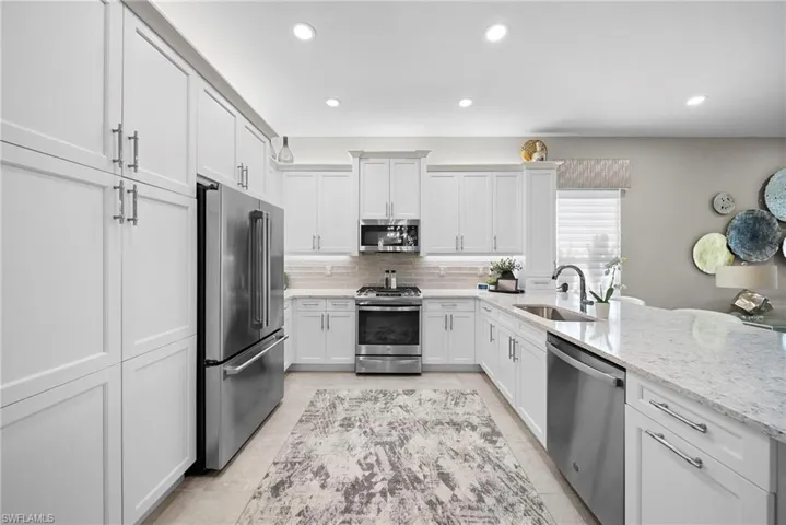 Kitchen featuring stainless steel appliances, white cabinets, a peninsula, light stone counters, and recessed lighting