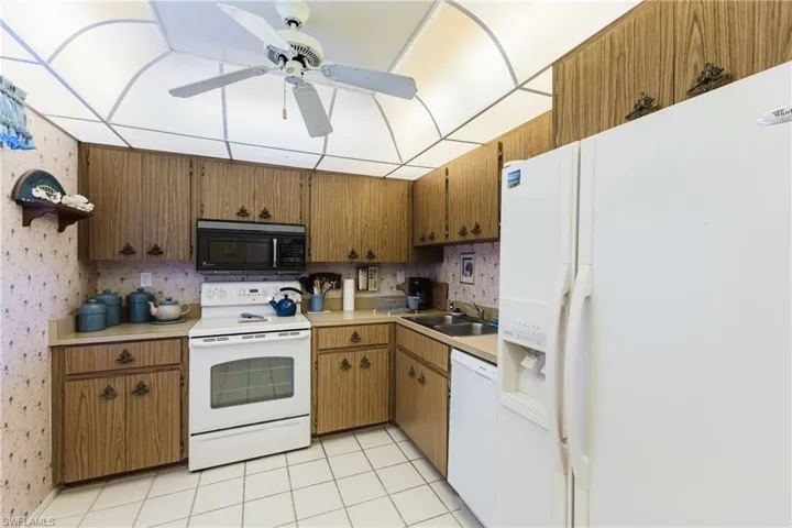 Galley-style kitchen featuring wood-finish cabinetry, white appliances including a refrigerator and electric range, tile flooring, and ample counter space