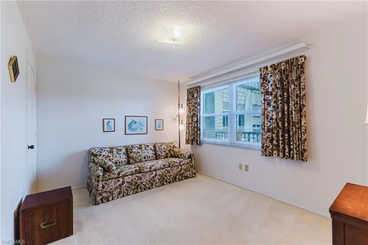 White walls with neutral carpeting, featuring a window with horizontal blinds, and a white ceiling