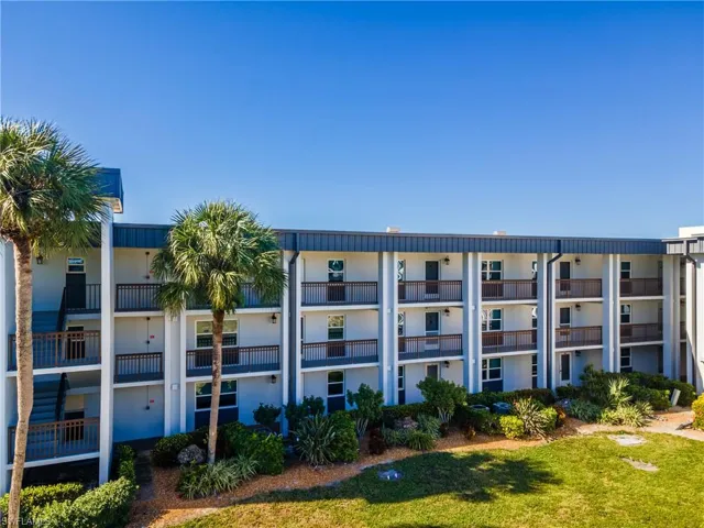 Multi-level building exterior featuring multiple private balconies with dark railings, a dark roofline, and a manicured lawn area