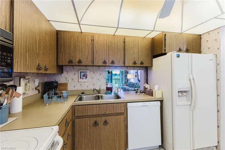 Wood-finish cabinetry, double basin stainless steel sink, integrated dishwasher, and a pass-through window