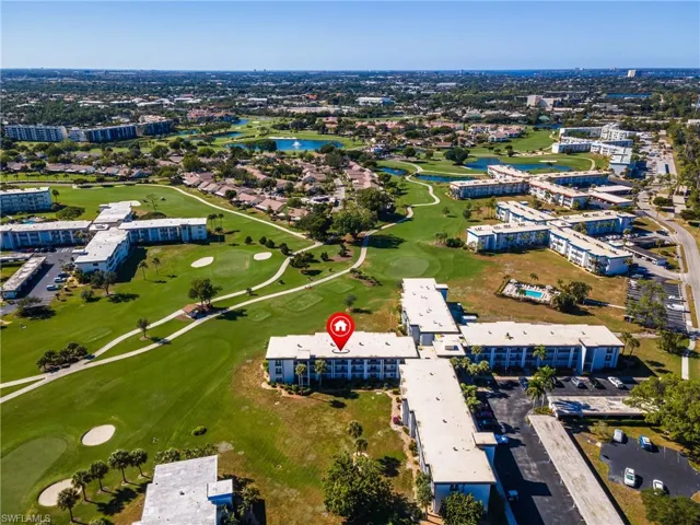 Aerial perspective of the property, featuring a multi-building complex with flat roofs, surrounded by expansive green spaces and golf course elements