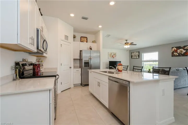 Kitchen with white cabinetry, appliances with stainless steel finishes, an island with sink, ceiling fan, and light tile floors