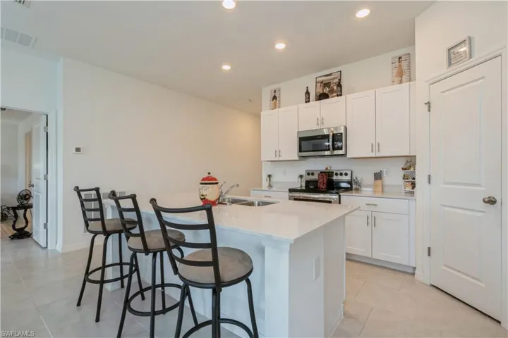 Kitchen featuring stainless steel appliances, white cabinetry, an island with sink, sink, and light tile floors