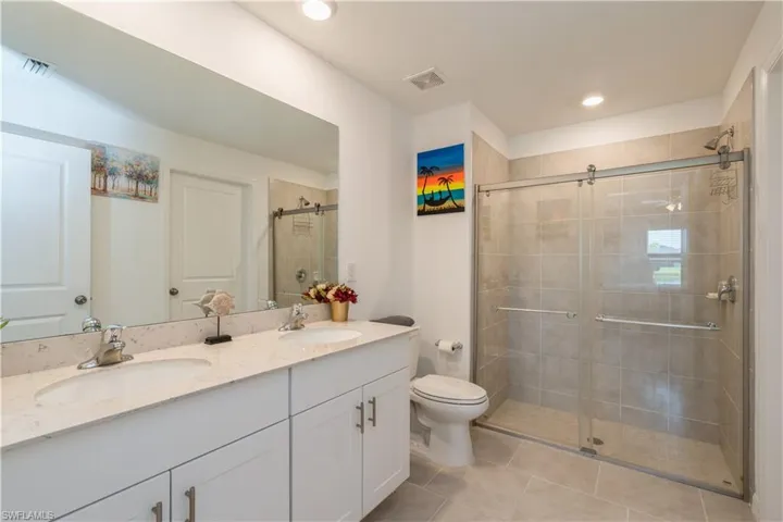 Bathroom featuring walk in shower, double vanity, toilet, and tile floors