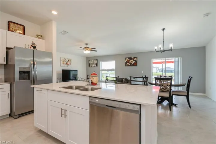 Kitchen featuring decorative light fixtures, ceiling fan with notable chandelier, stainless steel appliances, a center island with sink, and sink