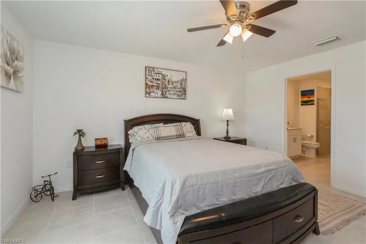 Bedroom with ensuite bathroom, ceiling fan, and light tile floors