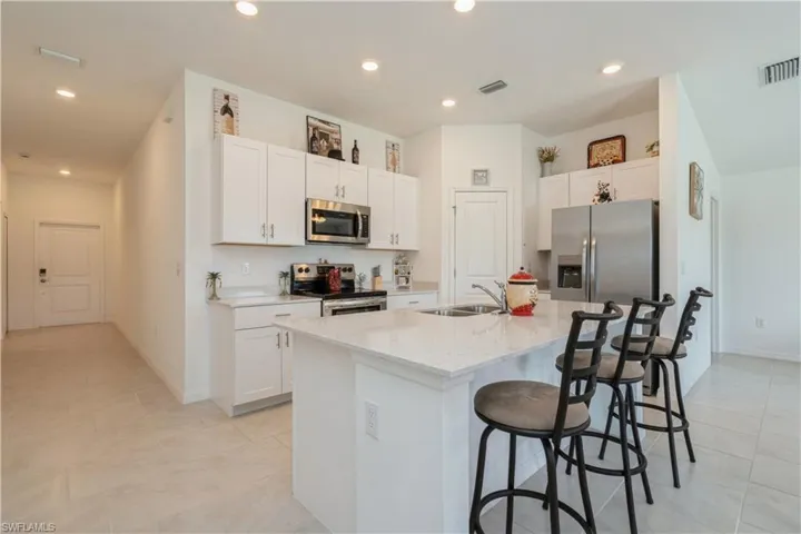 Kitchen featuring light tile flooring, stainless steel appliances, an island with sink, white cabinets, and a breakfast bar
