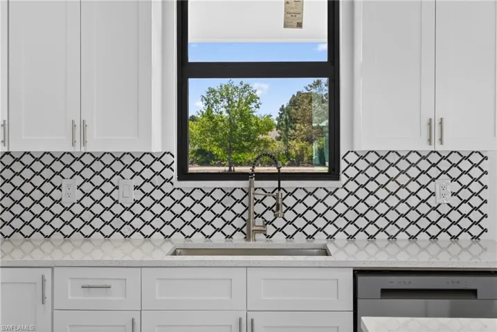Kitchen featuring white cabinets, light stone countertops, and stainless steel dishwasher