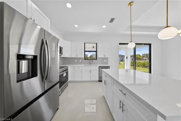 Kitchen with stainless steel appliances, white cabinets, light stone counters, backsplash, and decorative light fixtures