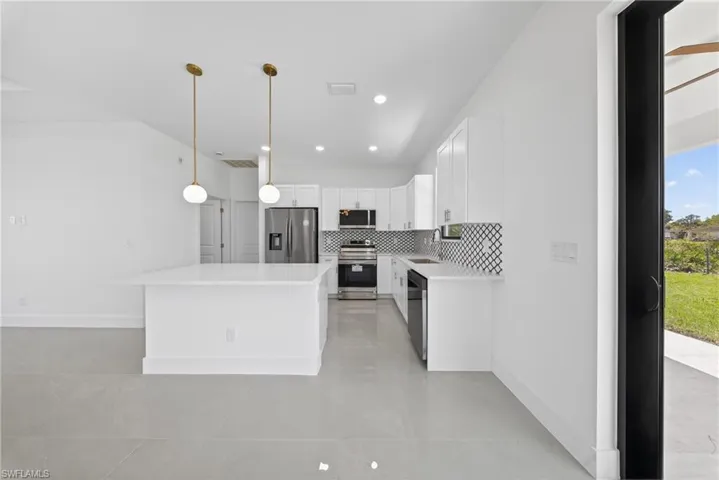 Kitchen featuring white cabinets, stainless steel appliances, a kitchen island, light stone countertops, and decorative backsplash
