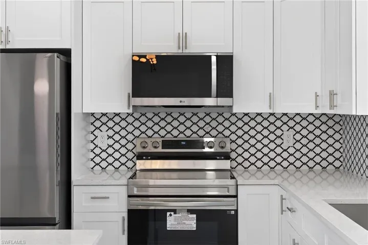 Kitchen with stainless steel appliances, white cabinets, light stone counters, and backsplash