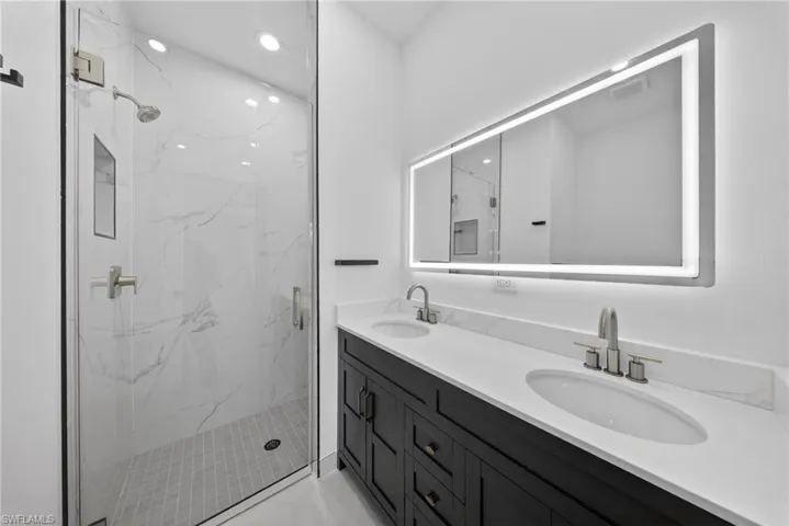 Full bathroom with double vanity, a marble finish shower, and recessed lighting