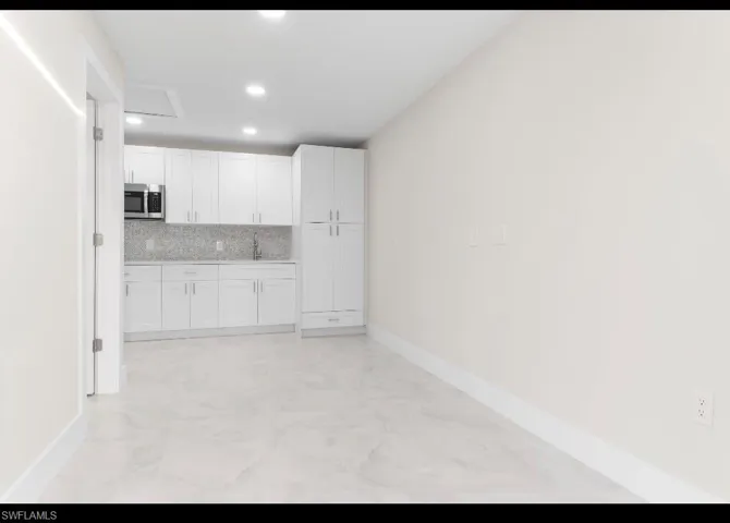 Kitchen with white cabinetry, stainless steel microwave, recessed lighting, tasteful backsplash, and light stone counters