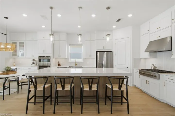 Gourmet kitchen with an expansive island, white shaker cabinetry, stainless steel appliances, and light wood-finish flooring
