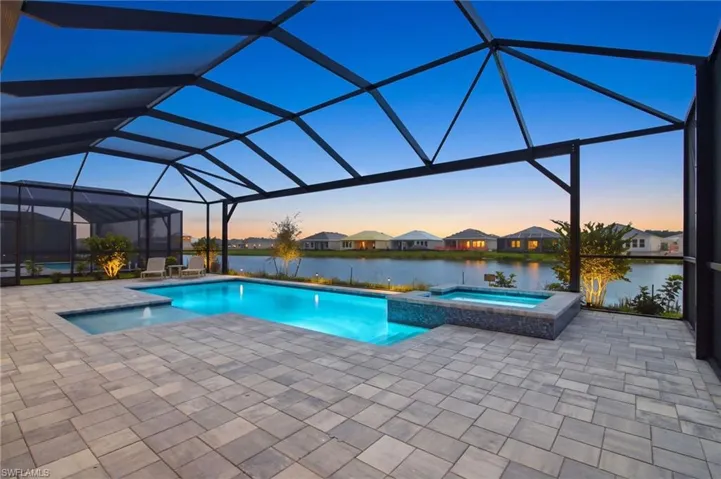 Screened-in paver patio featuring a swimming pool, integrated spa, and illuminated landscaping overlooking a body of water