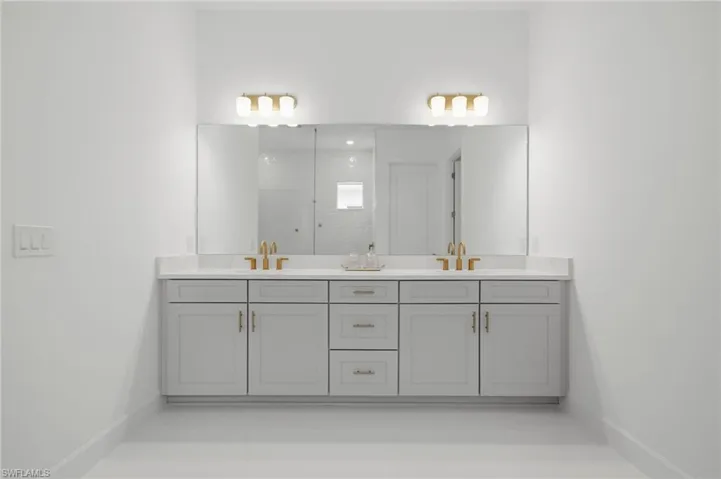 Dual vanity with light gray cabinetry, gold-finish hardware, and a single large mirror