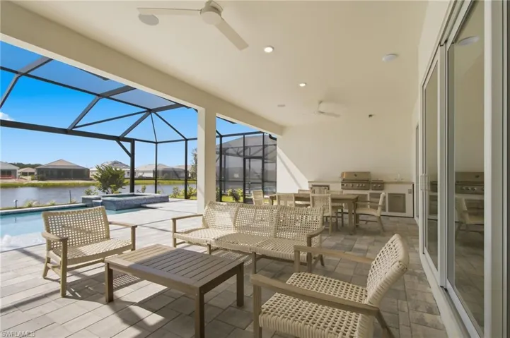 Screened lanai with paver flooring, built-in outdoor kitchen, ceiling fans, and integrated swimming pool with spa