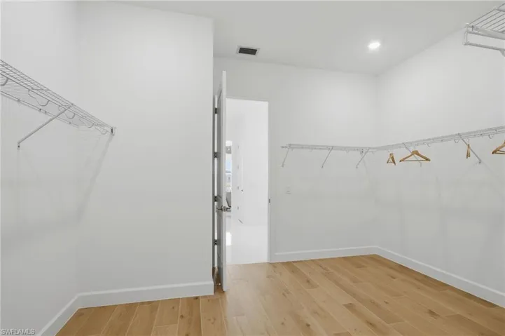 Spacious walk-in closet featuring wood-finish flooring, white walls, recessed lighting, and wire shelving