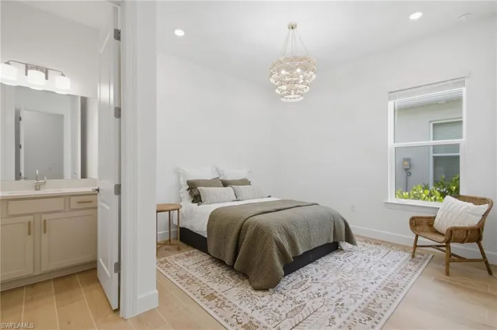 Recessed ceiling lighting, decorative tiered chandelier, large window with roller shade, wood-finish flooring, and a single vanity with a countertop