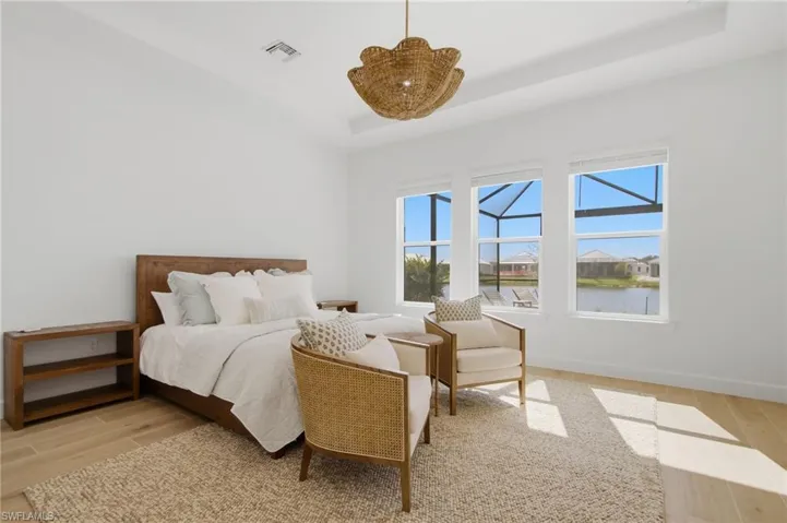 Tray ceiling with an organic-inspired lighting fixture, wood-finish flooring, and multiple windows offering water views