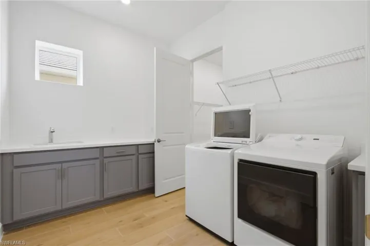 Laundry area featuring wood-finish flooring, a utility sink with a stainless steel faucet, and gray cabinetry with a light-toned countertop