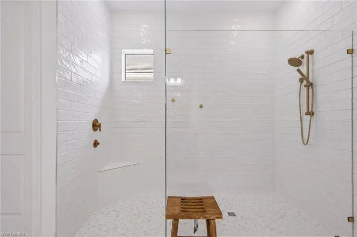 Spacious shower enclosure with clear glass paneling, white subway tile walls, and a built-in corner bench