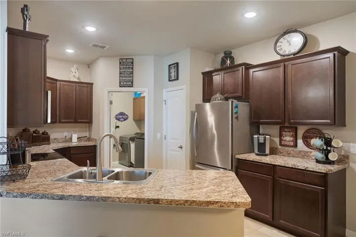 Kitchen with freestanding refrigerator, dark brown cabinetry, a peninsula, light countertops, and recessed lighting