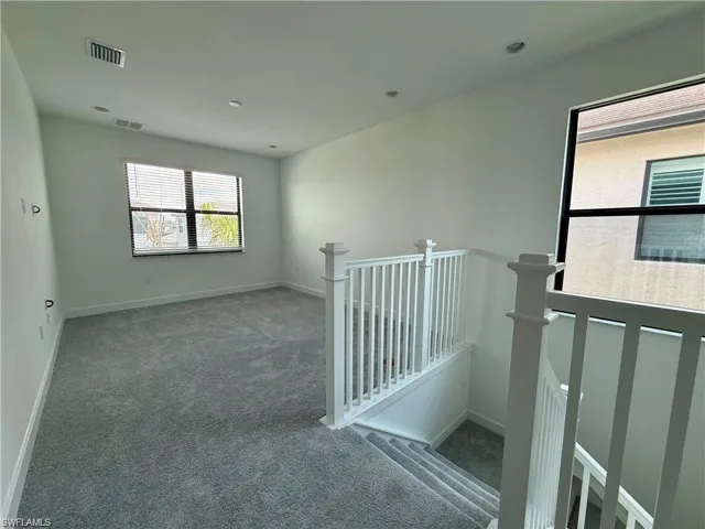 Upper-level space featuring light gray carpeting, white walls, recessed lighting, and two large windows with horizontal blinds