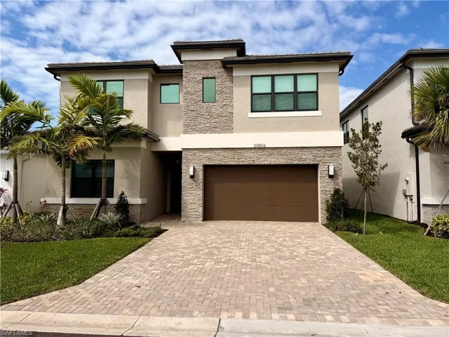 Contemporary two-story exterior with stone veneer accents, stucco siding, a paver driveway, an integrated two-car garage, and mature landscaping
