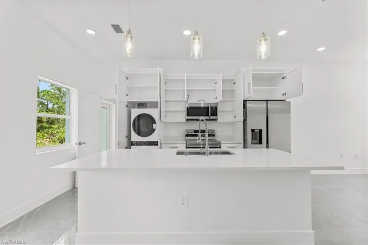 Kitchen featuring appliances with stainless steel finishes, open shelves, white cabinetry, stacked washer and clothes dryer, and recessed lighting