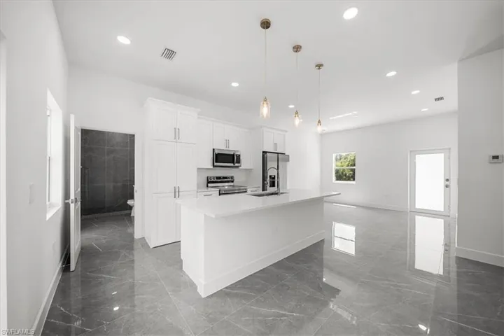Kitchen featuring appliances with stainless steel finishes, marble tiled floors, an island with sink, white cabinetry, and recessed lighting