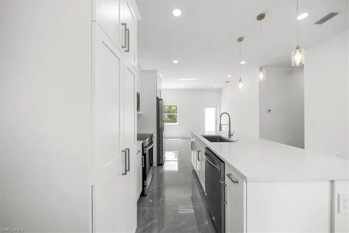 Kitchen featuring appliances with stainless steel finishes, an island with sink, white cabinets, light countertops, and recessed lighting