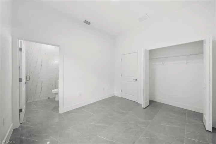 Unfurnished bedroom featuring marble finish flooring, a closet, and ensuite bath