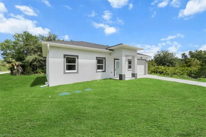 View of front of property with a front yard, an attached garage, concrete driveway, and stucco siding