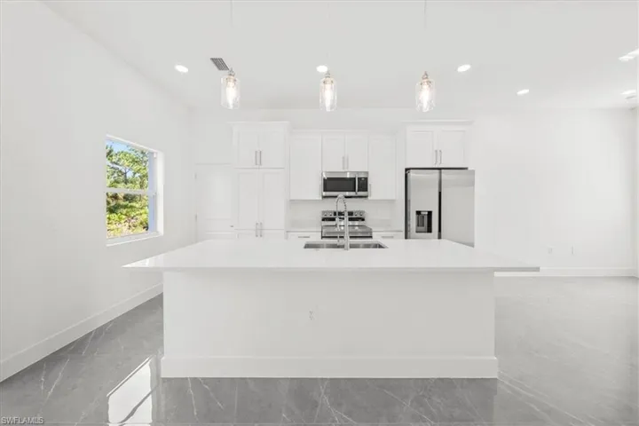 Kitchen with appliances with stainless steel finishes, an island with sink, light countertops, white cabinetry, and recessed lighting