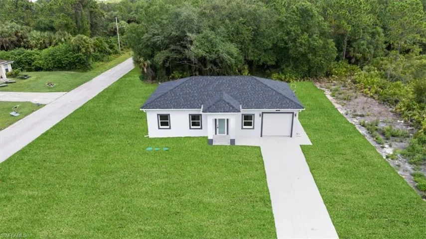 View of front facade featuring driveway, stucco siding, a front lawn, an attached garage, and roof with shingles