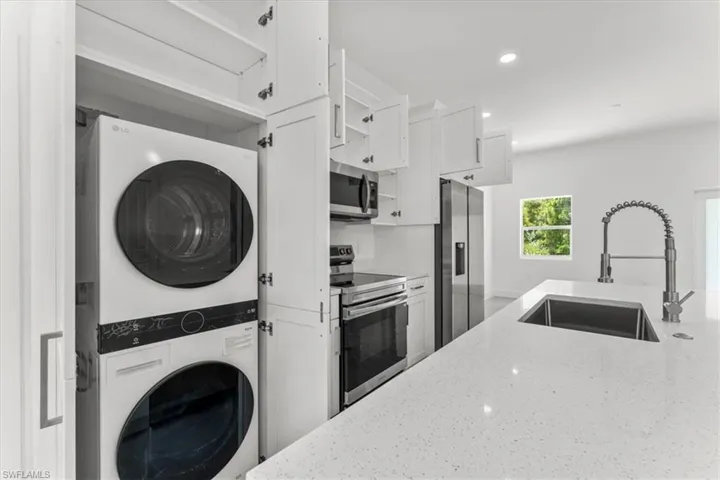 Kitchen featuring stainless steel appliances, stacked washer / dryer, open shelves, light stone counters, and recessed lighting