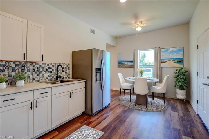 Kitchen with tasteful backsplash, a sink, stainless steel refrigerator with ice dispenser, white cabinetry, and visible vents