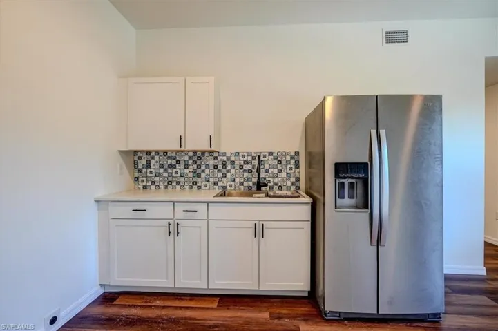 Kitchen with a sink, white cabinets, dark wood finished floors, stainless steel refrigerator with ice dispenser, and visible vents