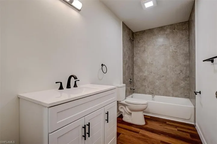 Full bath with shower / tub combination, wood finished floors, vanity, and toilet