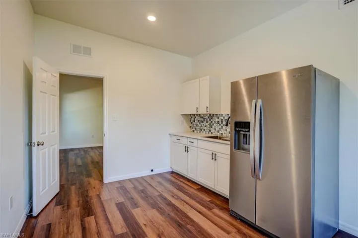 Kitchen with white cabinets, visible vents, stainless steel fridge, tasteful backsplash, and dark wood-style flooring